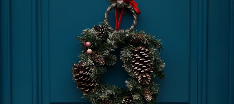 a photo of a green wreath with pinecones on a blue door.